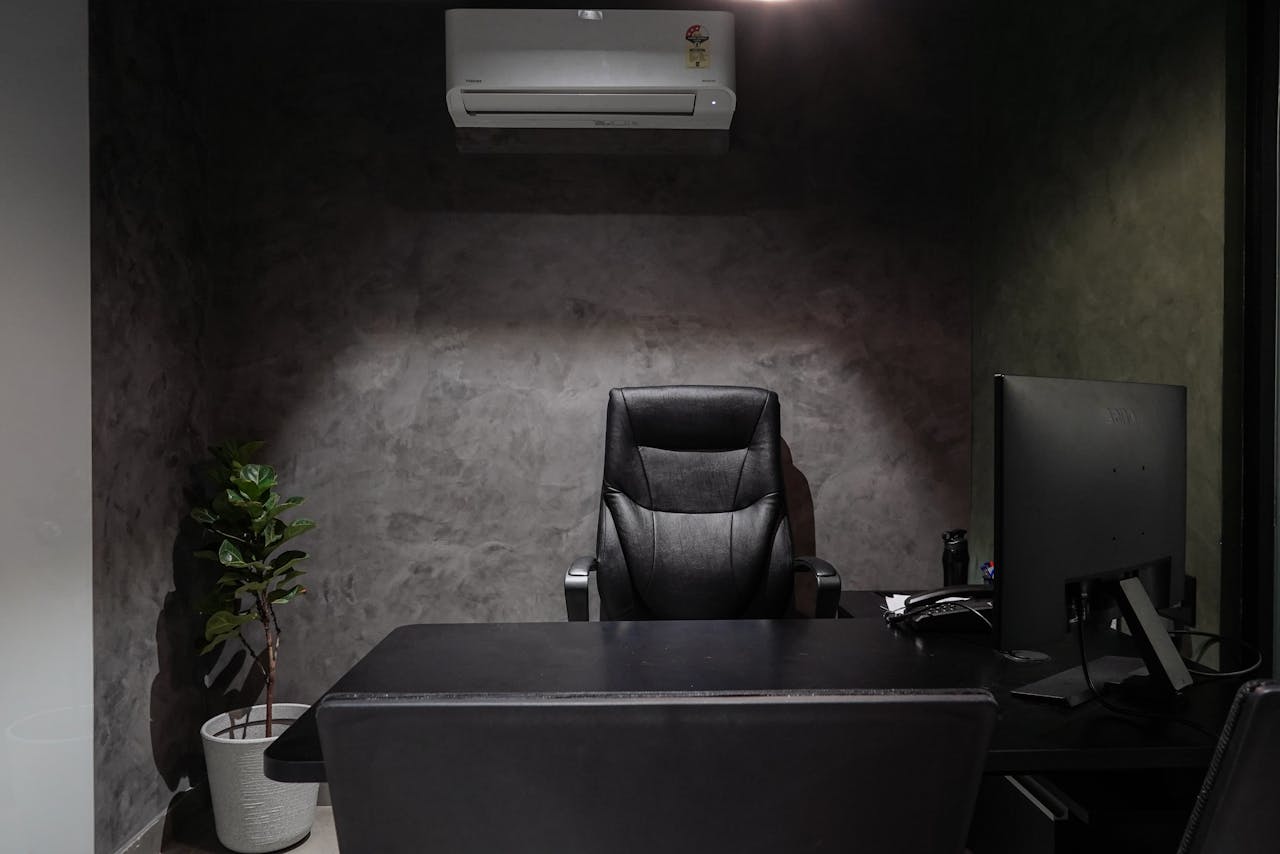 Minimalist office interior featuring leather chair, desk, monitor, plant, and air conditioner.